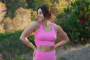 Woman in pink athletic wear standing on a trail with greenery in the background